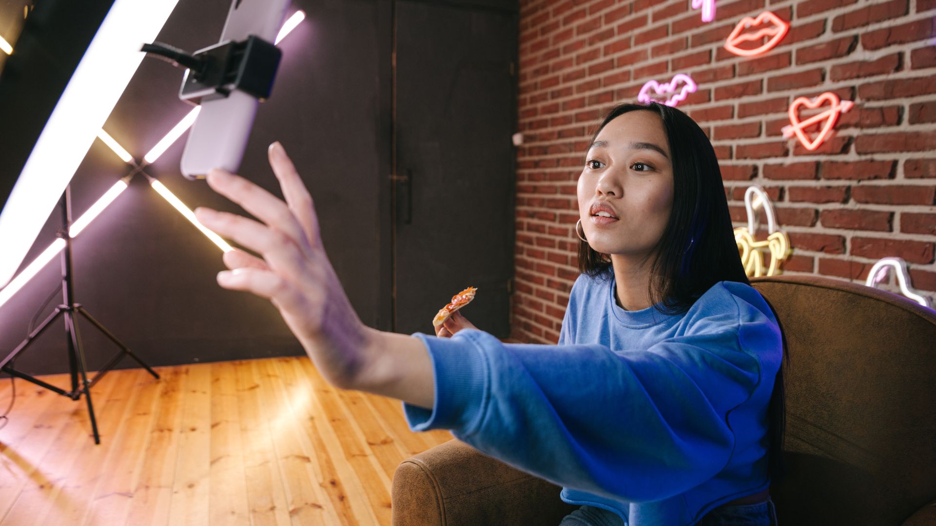 Young woman taking selfie with phone near lighting equipment and neon signs
