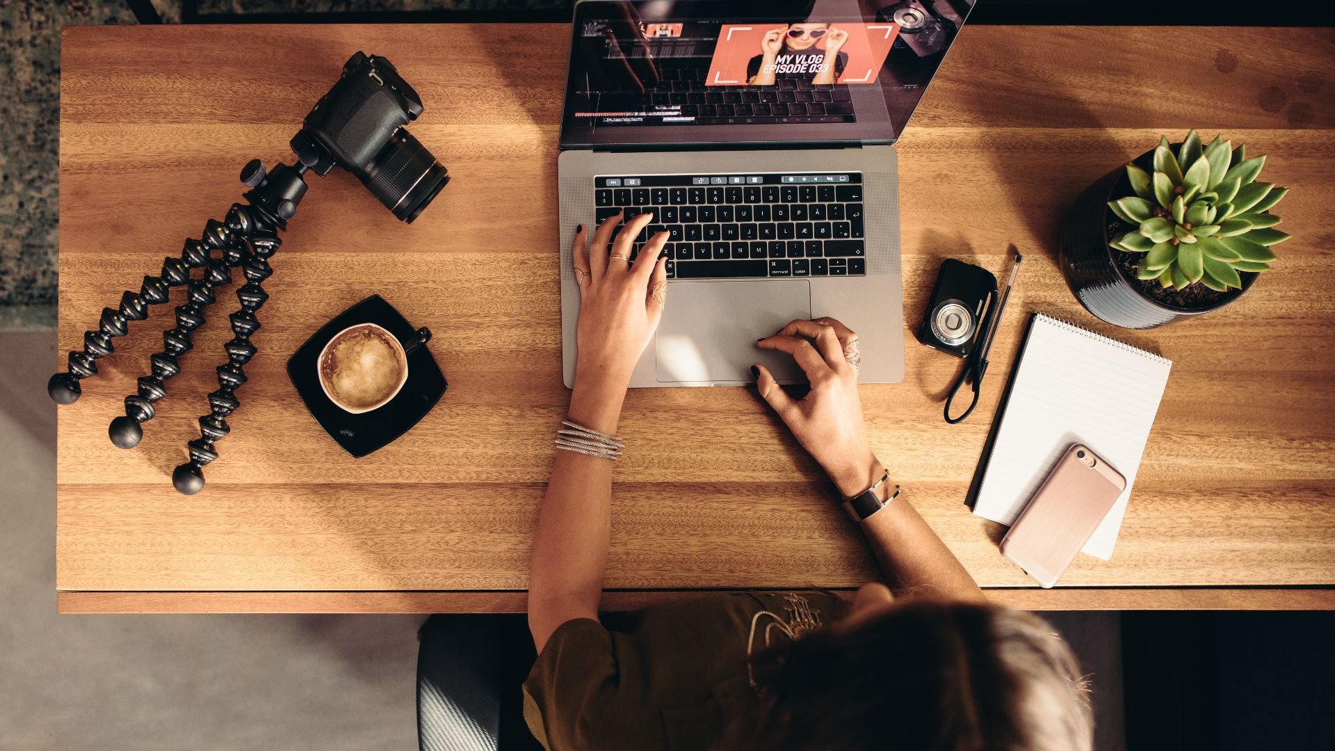 Creative workspace with camera, laptop, coffee, and plant on wooden desk